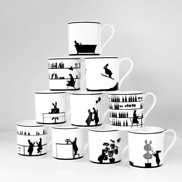 A set of white ceramic mugs with various black-and-white comic strip designs, including characters and scenarios such as a rabbit.